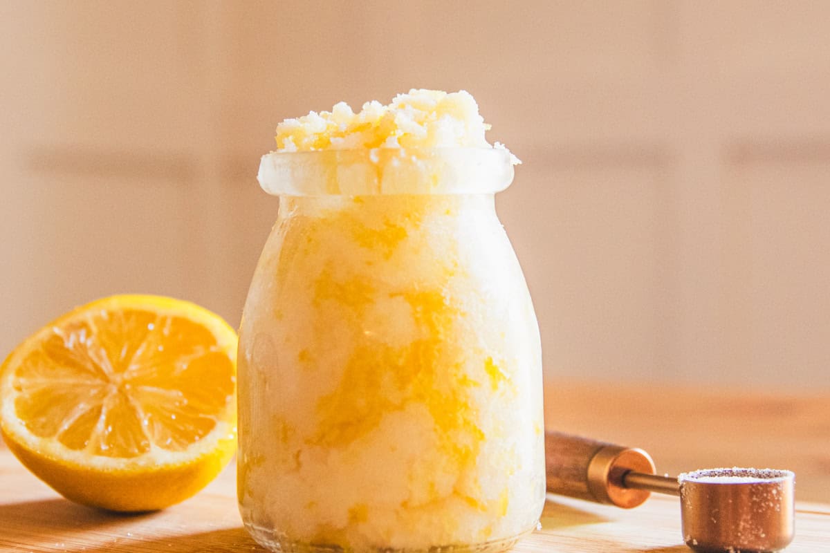 A jar of homemade hand scrub with a lemon half and a measuring spoon.