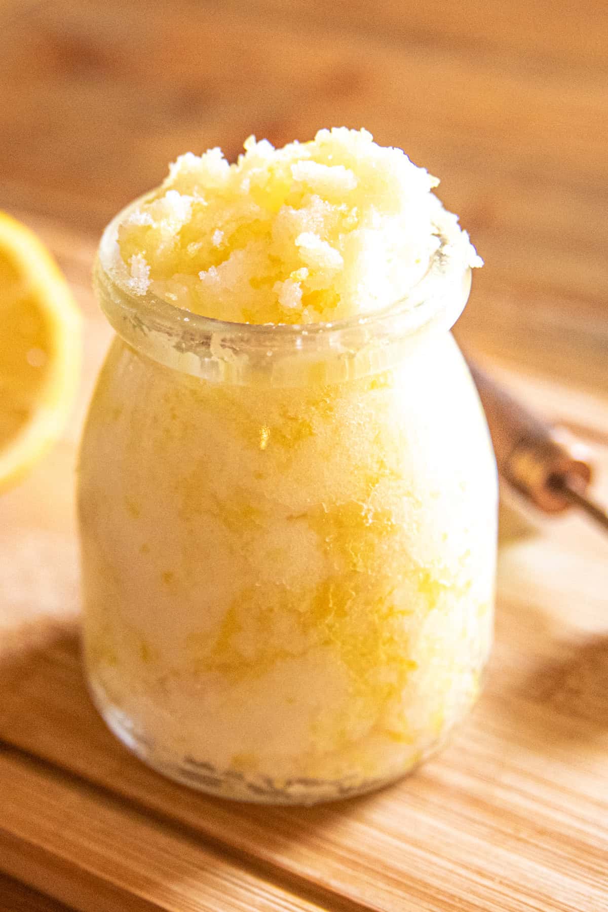 A jar of yellow hand scrub with a slice of lemon and a measuring spoon.