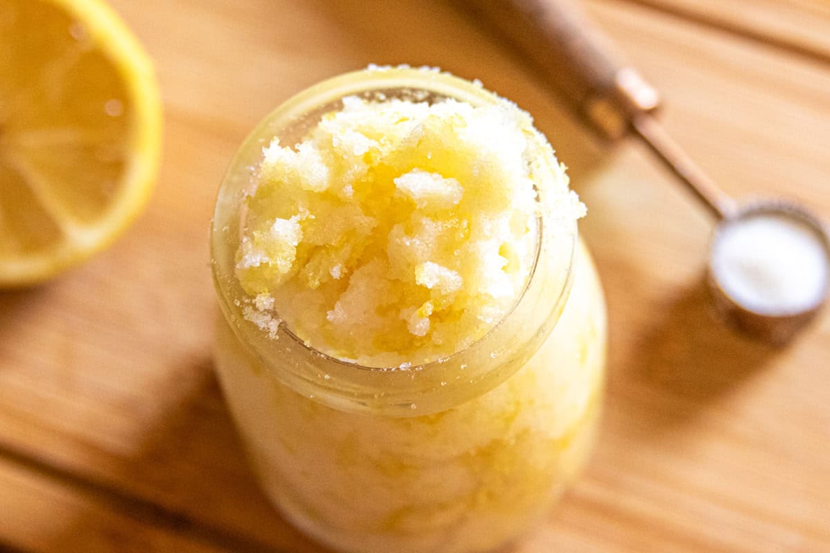 Looking down on a jar of homemade hand scrub with a measuring spoon and a fresh lemon.