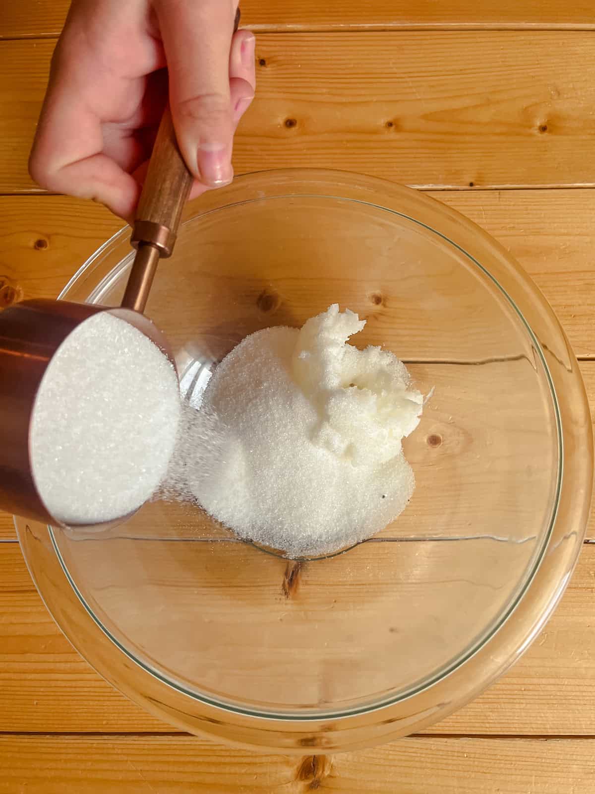 Pouring sugar into a bowl of coconut oil.