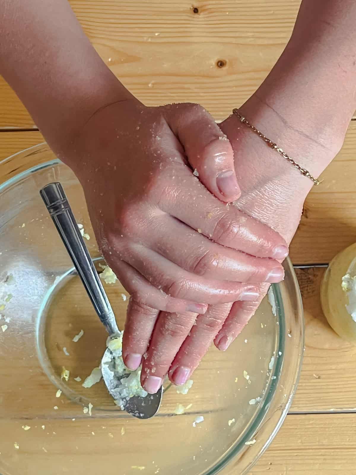 Scrubbing hands together over a bowl of homemade hand scrub.