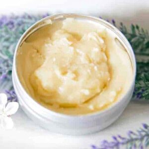 A homemade skin salve in a metal skin with several pieces of dried lavender next to it.