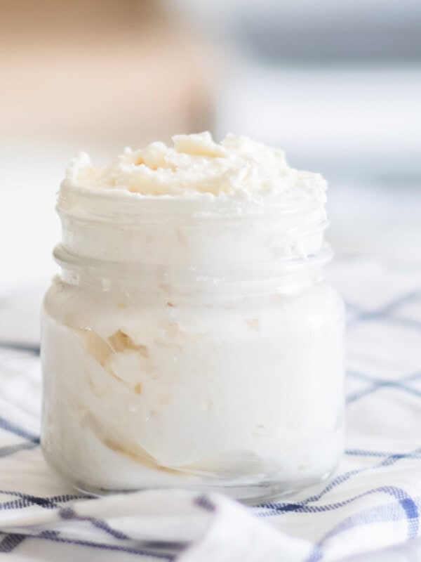 A jar of homemade shea butter lotion on a white and blue checkered towel.