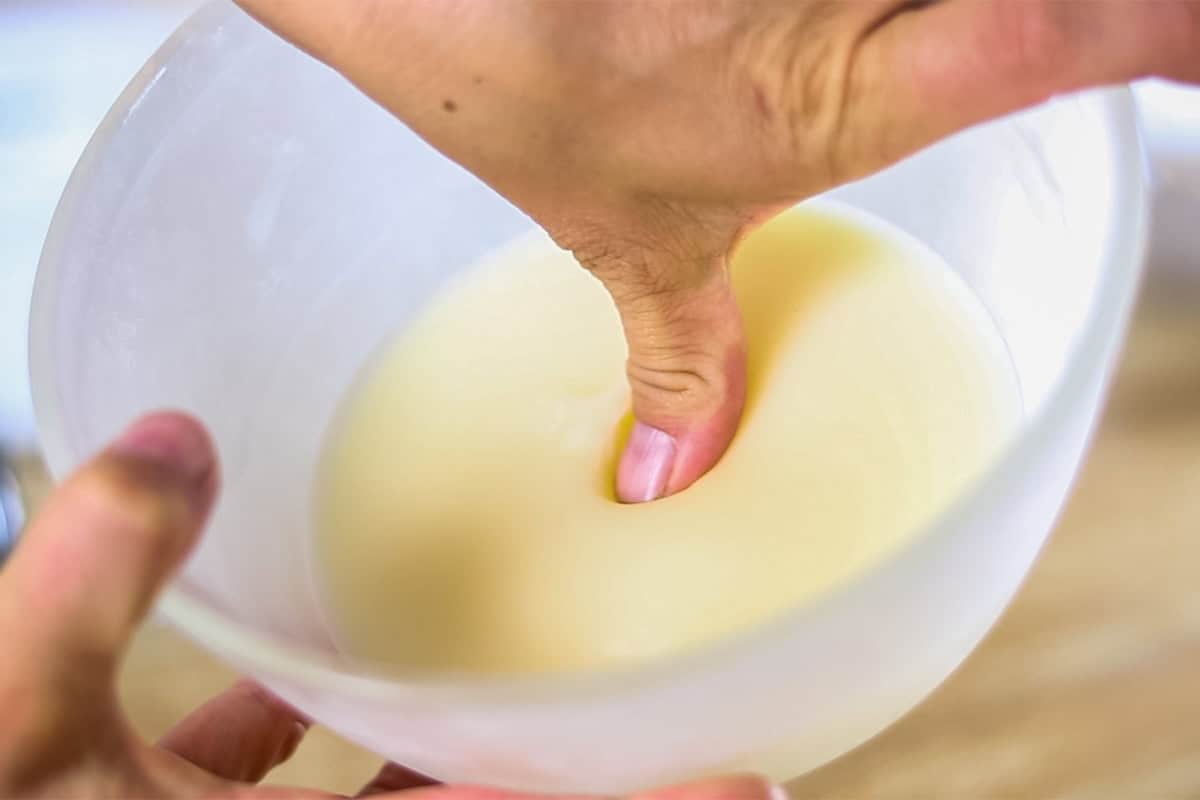 Pressing a fingertip into a bowl of hardened lotion mixture. 