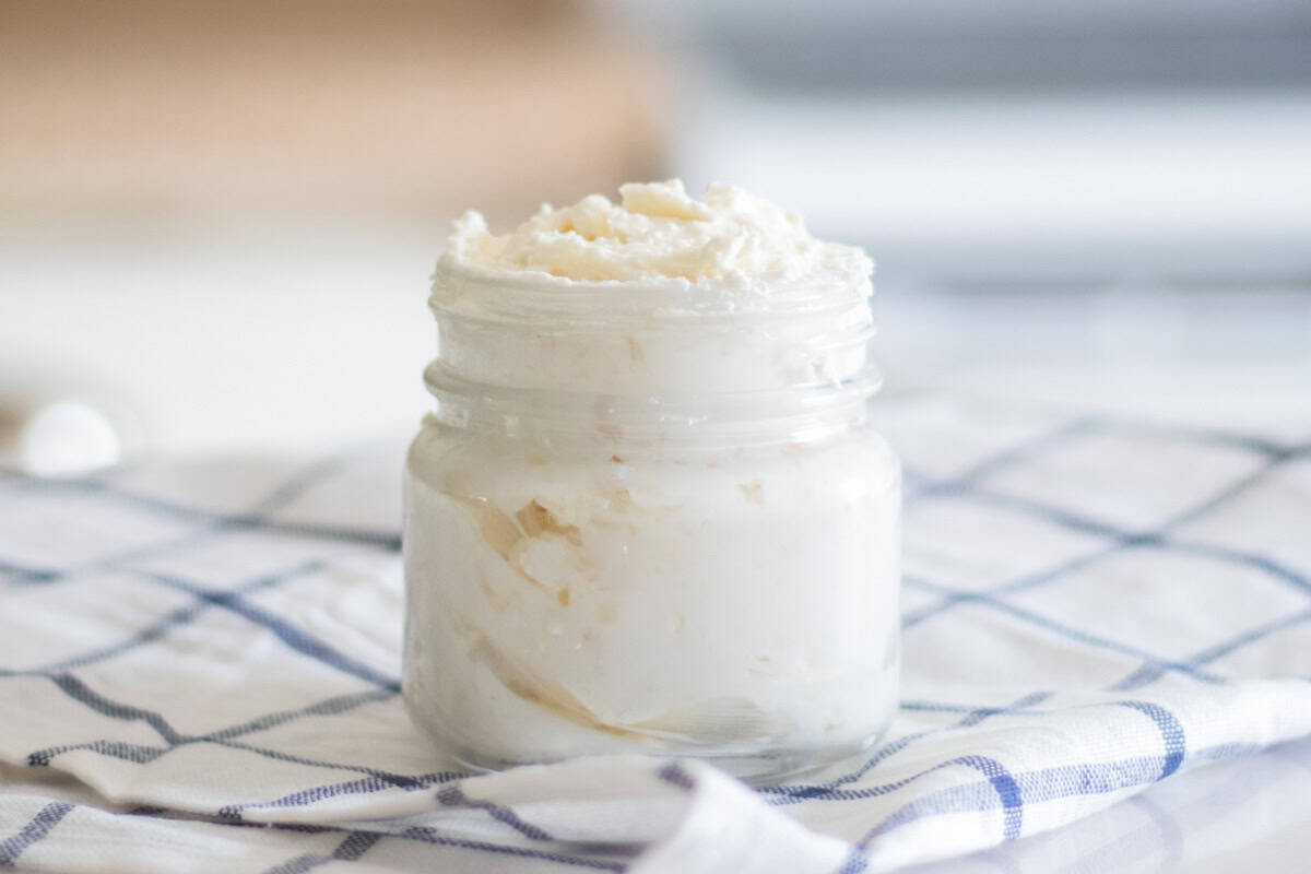 A jar of homemade shea butter lotion on a white and blue checkered tablecloth.