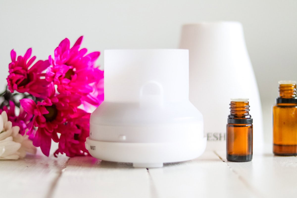 An essential oil diffuser with essential oil bottles and pink flowers.