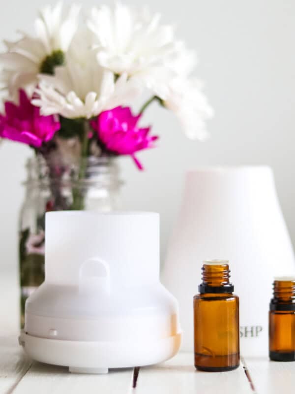 A diffuser with bottles of essential oils and fresh flowers.