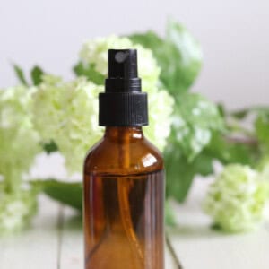 An amber spray bottle with fresh flowers around it.