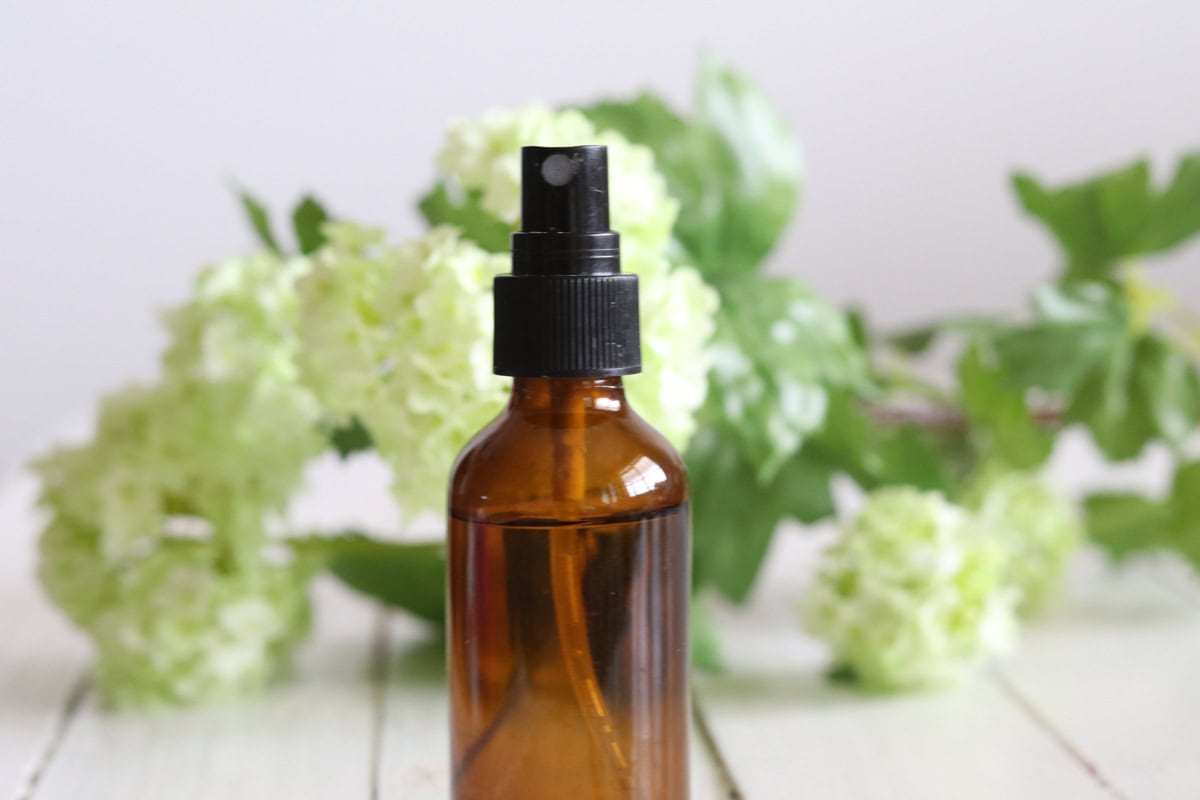 An amber spray bottle with fresh flowers around it.