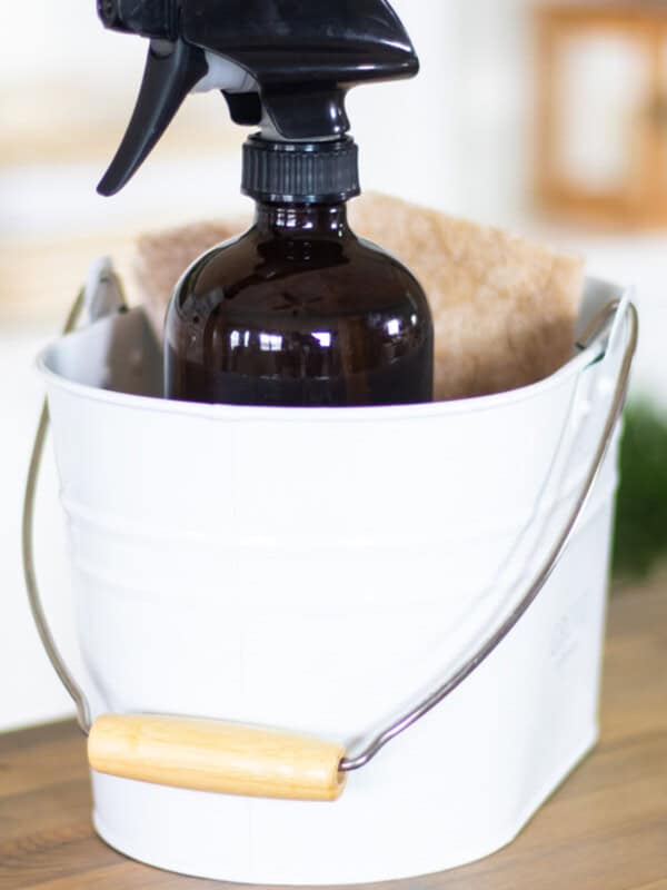 A white bucket with a glass spray bottle and a rag in it.