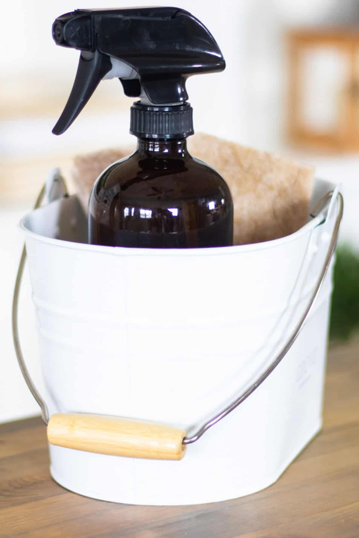A white bucket with a glass spray bottle and a rag in it.