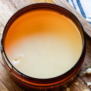 Homemade tallow balm in am amber jar on a wooden backdrop.