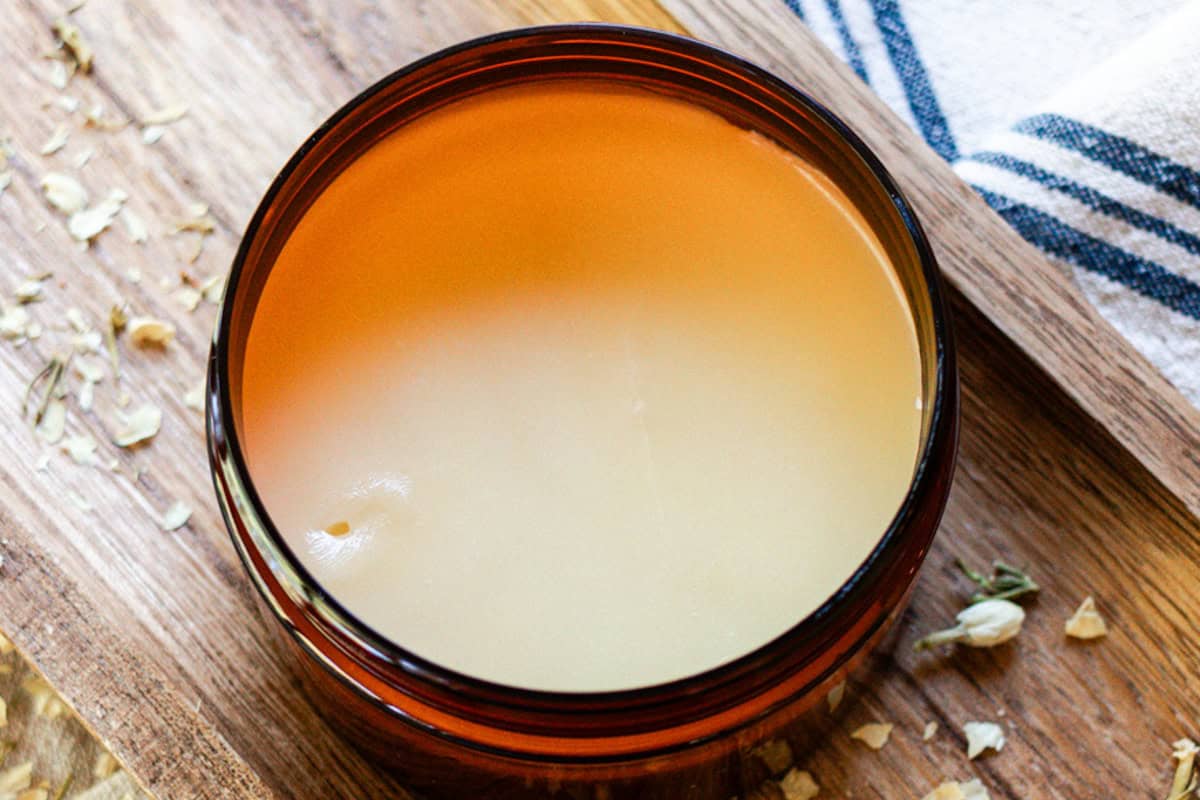 Homemade tallow balm in am amber jar on a wooden backdrop.