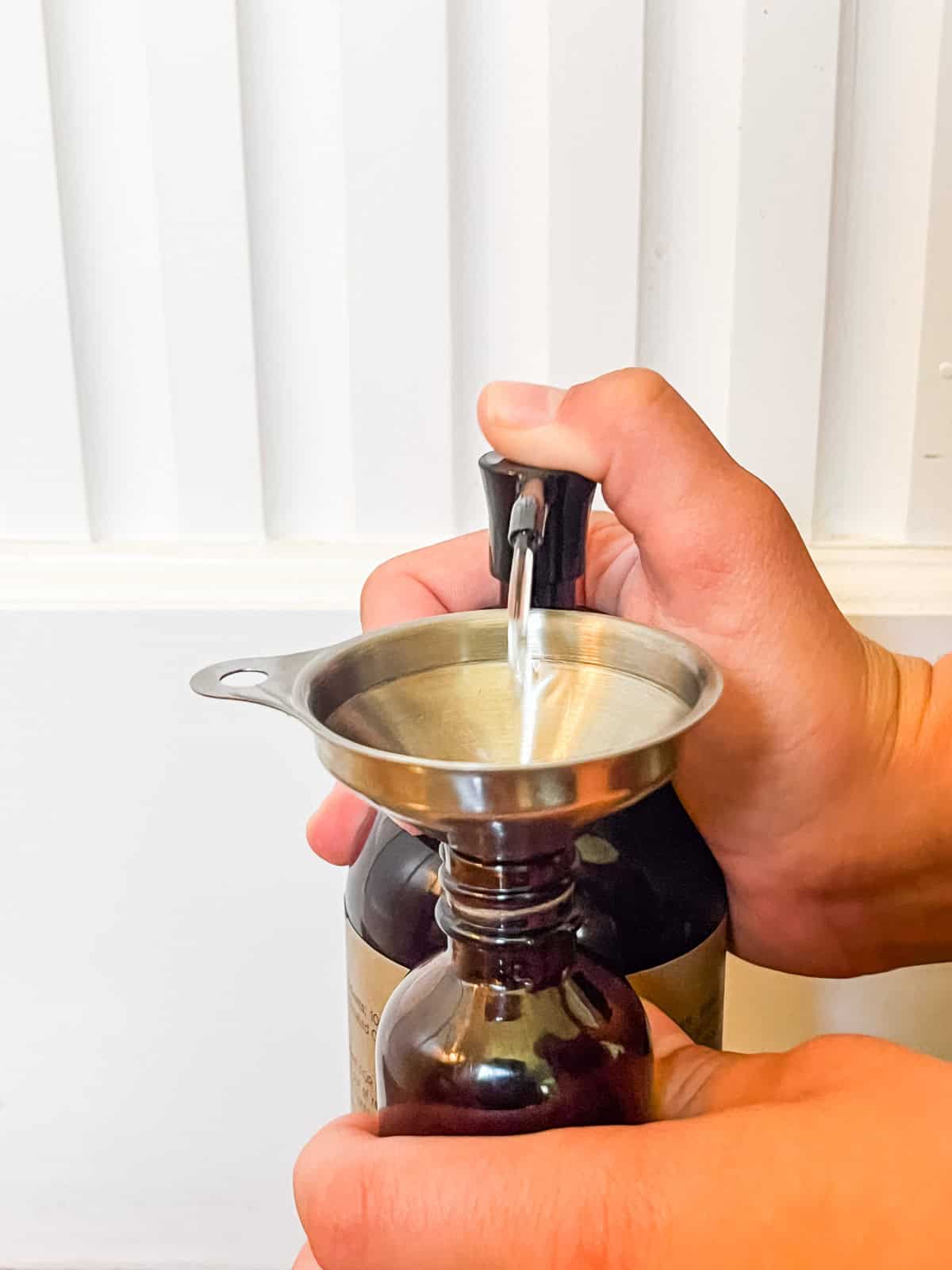 Squirting carrier oil into a glass bottle with a small funnel.