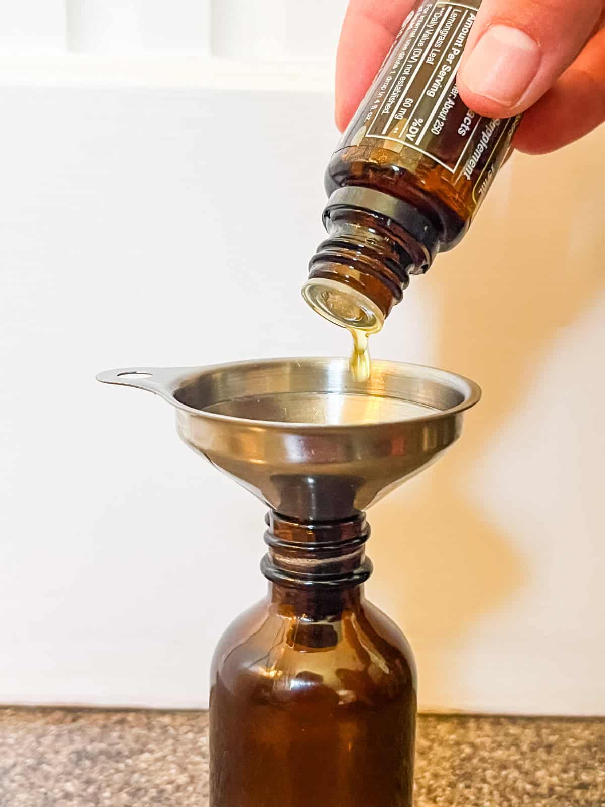 Dropping essential oils into a glass bottle with a small funnel.