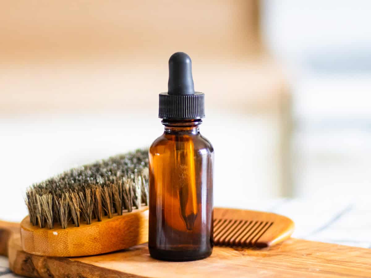 A bottle of homemade beard oil with a beard brush on a wooden board.