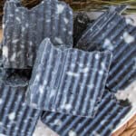 Bars of charcoal soap stacked up on a wicker placemat.