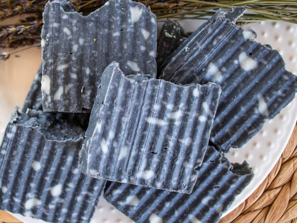 Bars of charcoal soap stacked up on a wicker placemat.