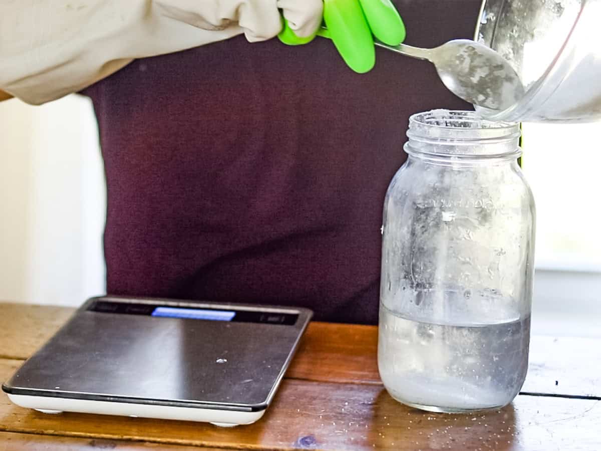 Scooping lye into a glass of water.