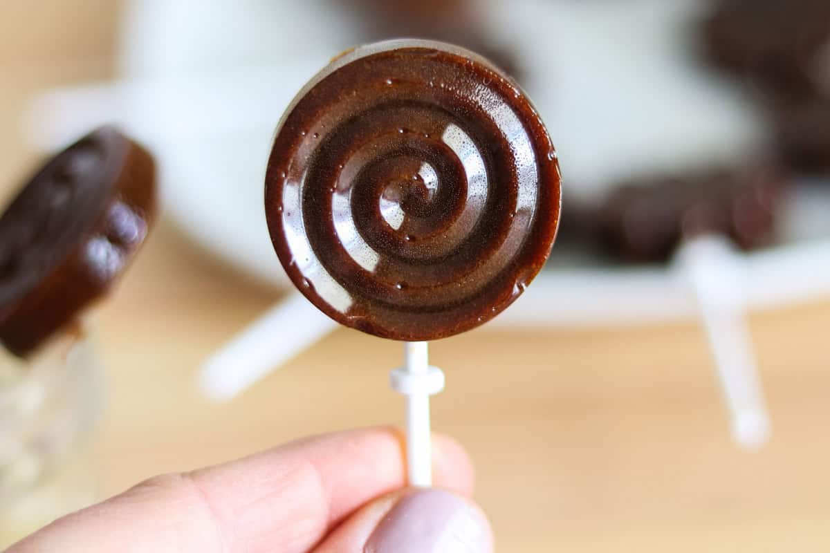Homemade lollipop being held above a plate of lollipops.
