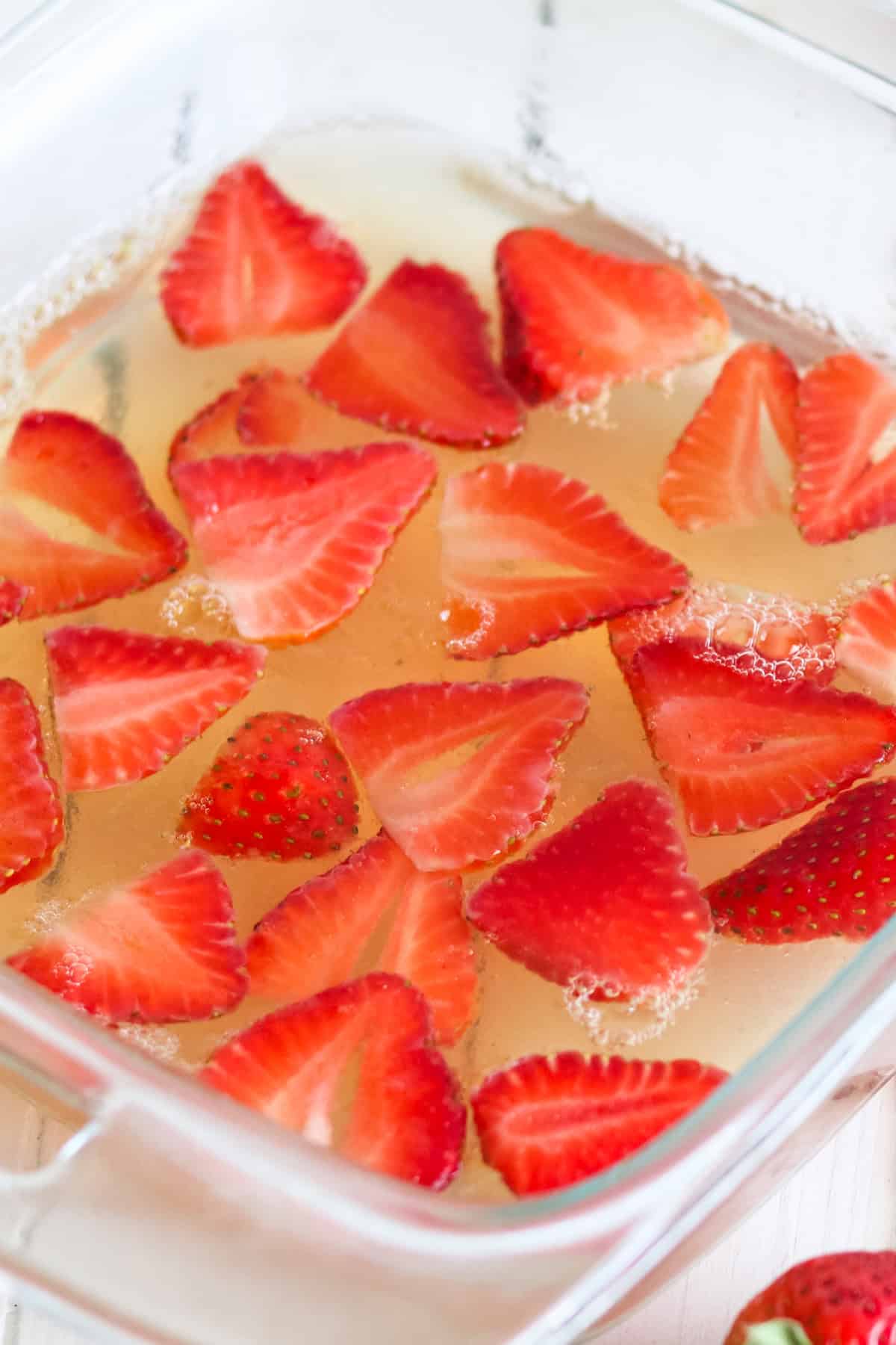 Sugar free jello in a glass dish with sliced strawberries in it.