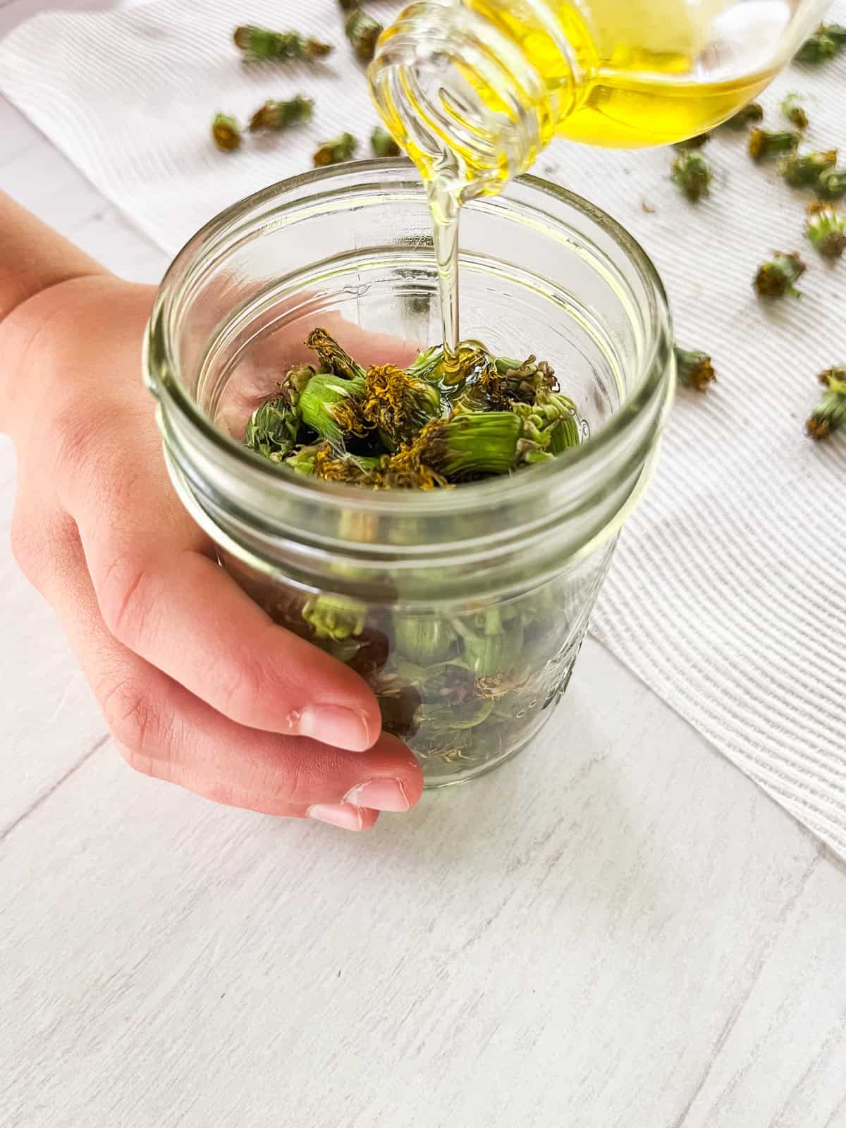 Pouring oil into a jar of dandelions.
