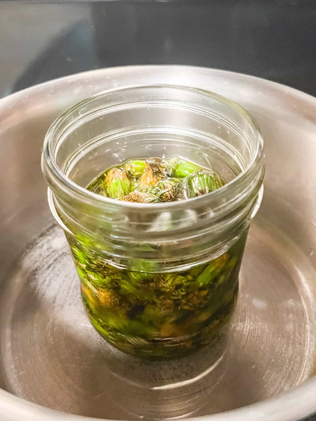 A jar of oil and dandelions in a pot of water.