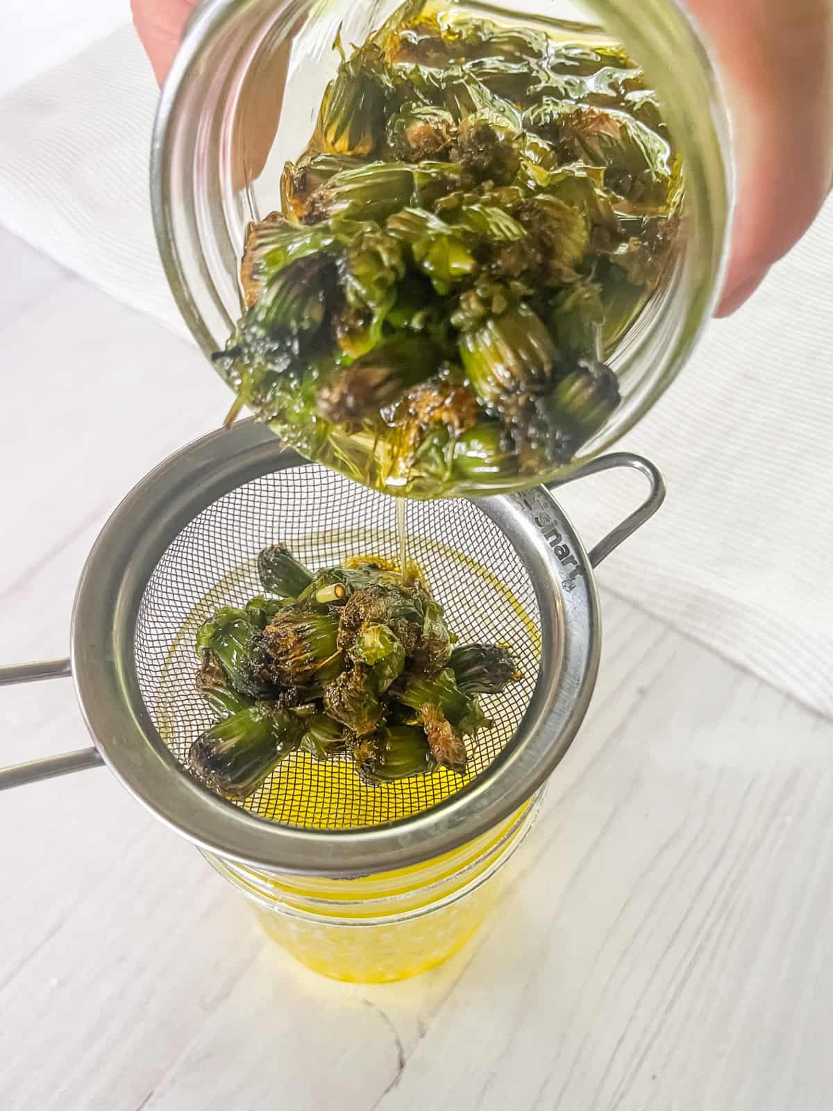 Pouring dandelions and oil through a fine mesh strainer.