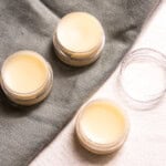 Three containers of tallow lip balm on a table with one empty container.