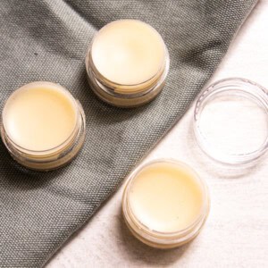 Three containers of tallow lip balm on a table with one empty container.