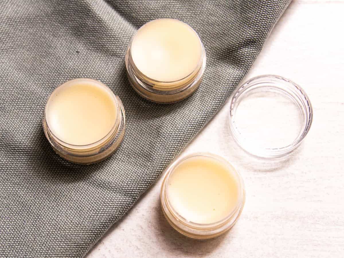 Three containers of tallow lip balm on a table with one lid.