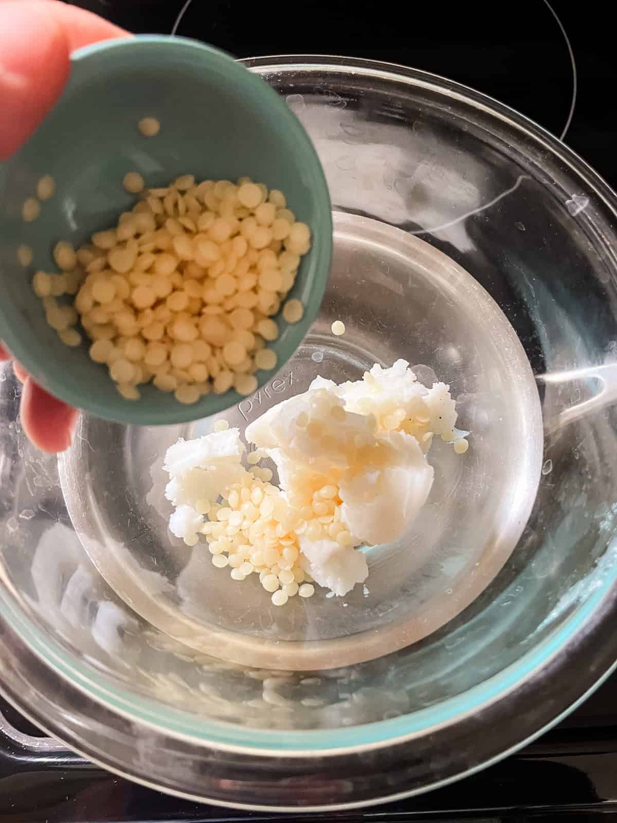 Pouring beeswax pellets into a double boiler with melting tallow.