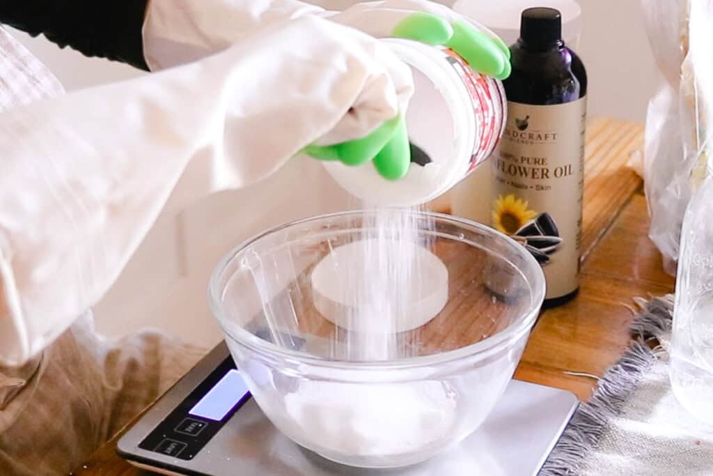 Measuring lye into a glass bowl with a digital scale and safety gloves.