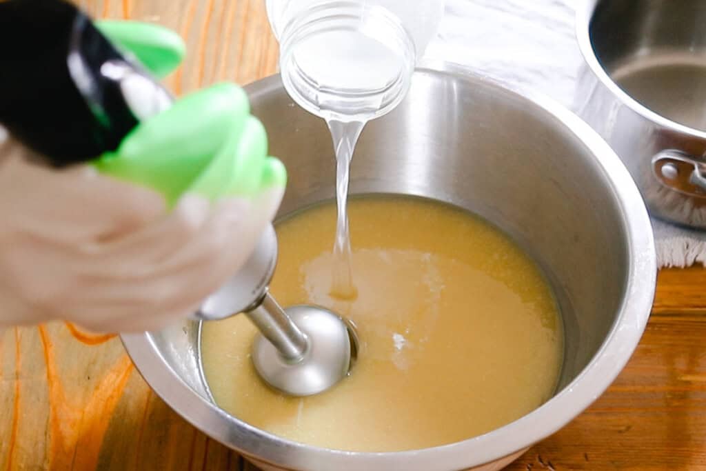 Blending soap with an immersion blender while pouring in lye and water.