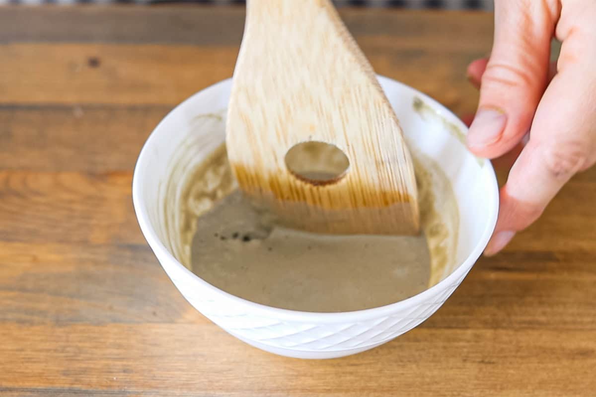 Stirring a bentonite clay mask with a wooden spoon.