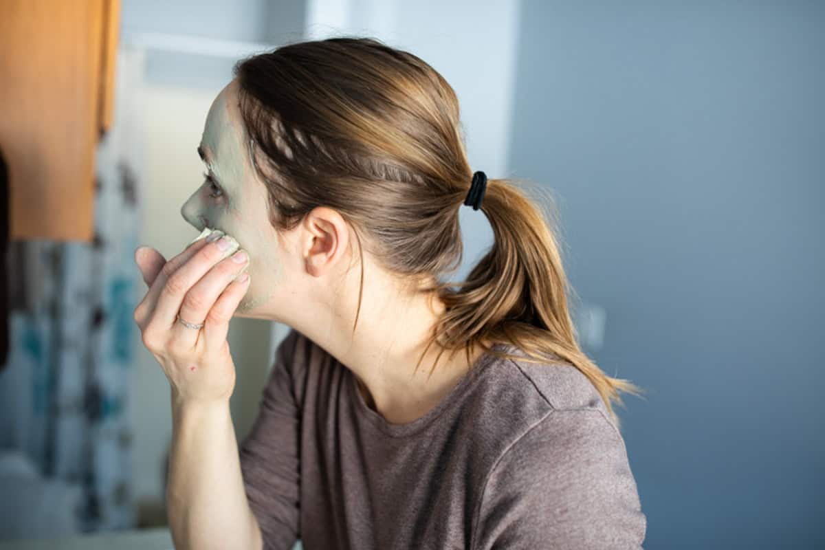 The author, Laura, applying a bentonite clay mask to her face in the bathroom with her hands. 