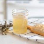 A jar of apple cider vinegar hair rinse with a hair brush and dried herbs.