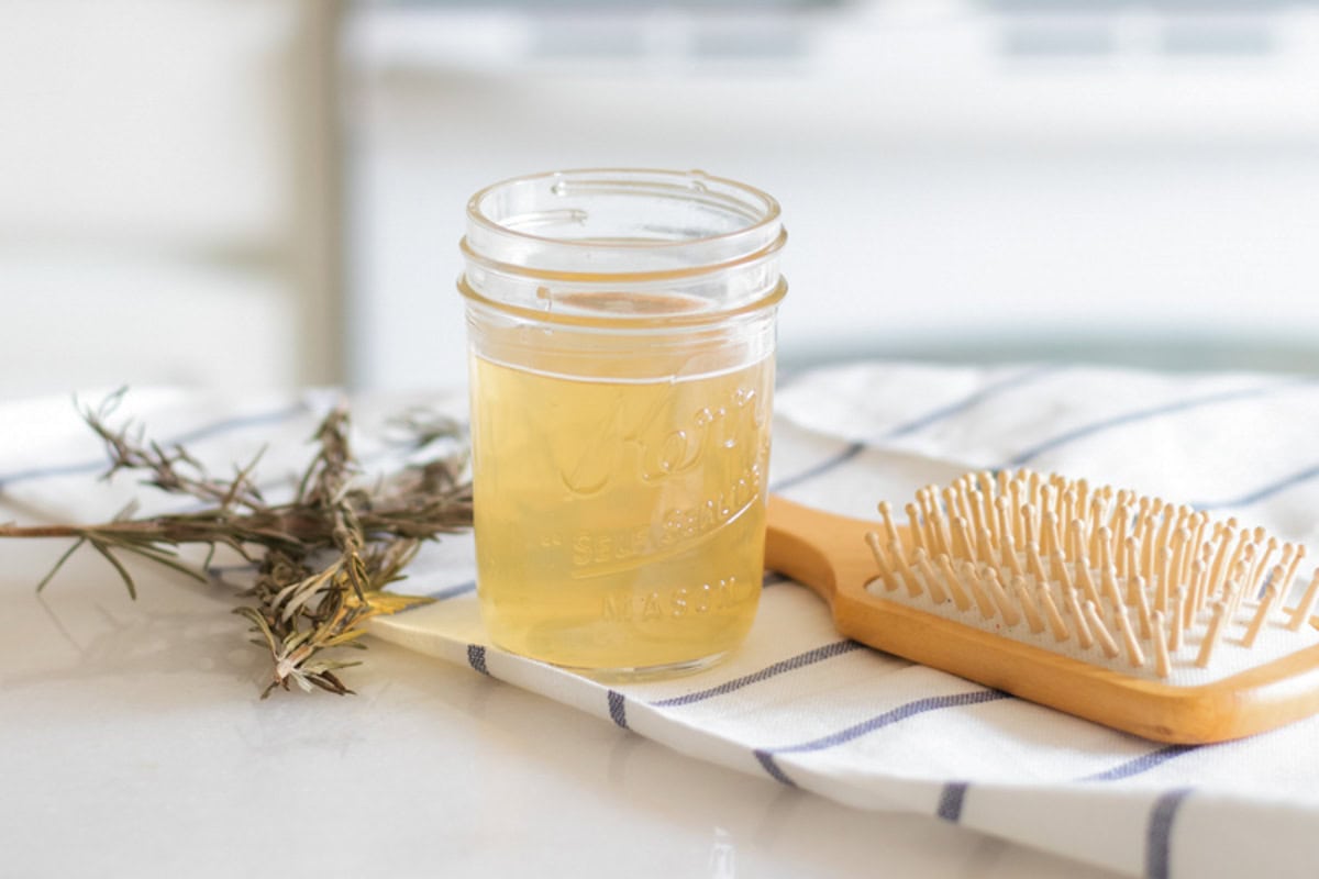 A jar of apple cider vinegar hair rinse with a hair brush and dried herbs.