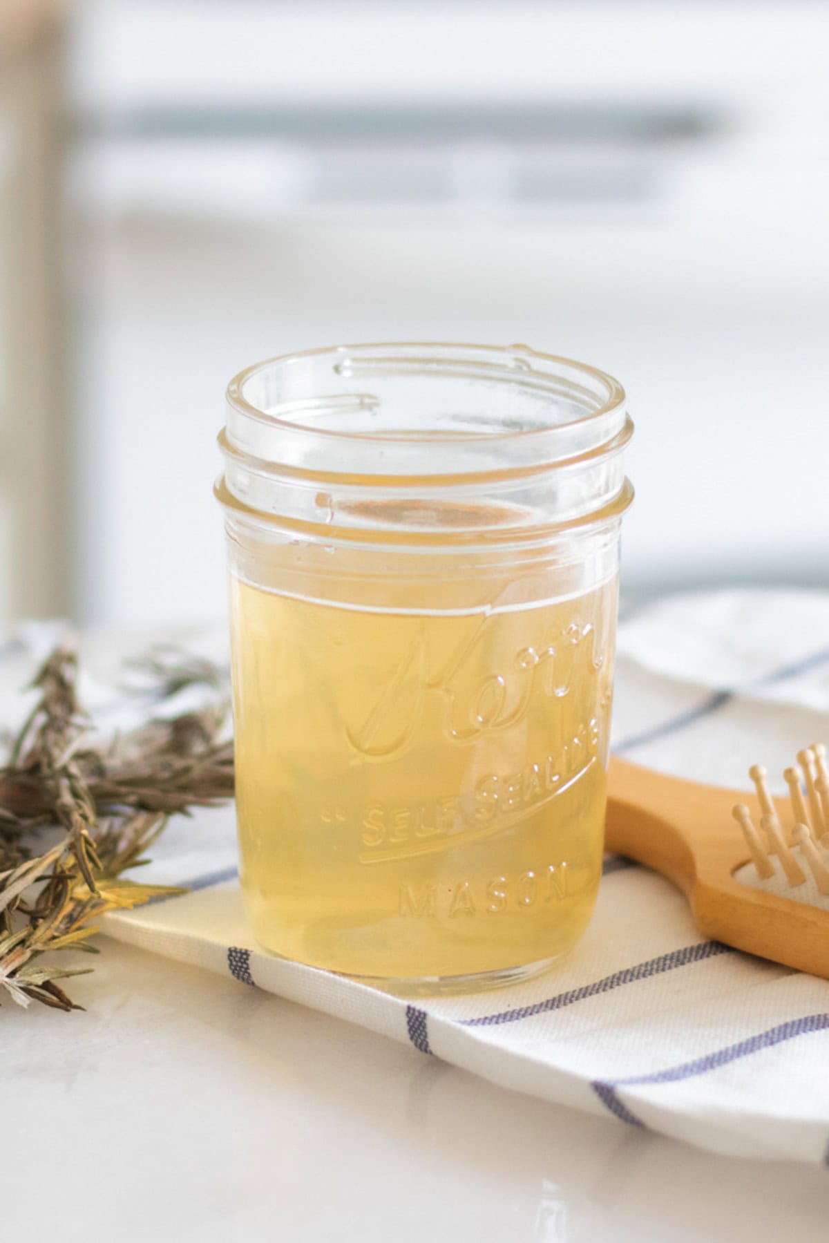 A jar of apple cider vinegar hair rinse on a striped towel with a hair brush. 