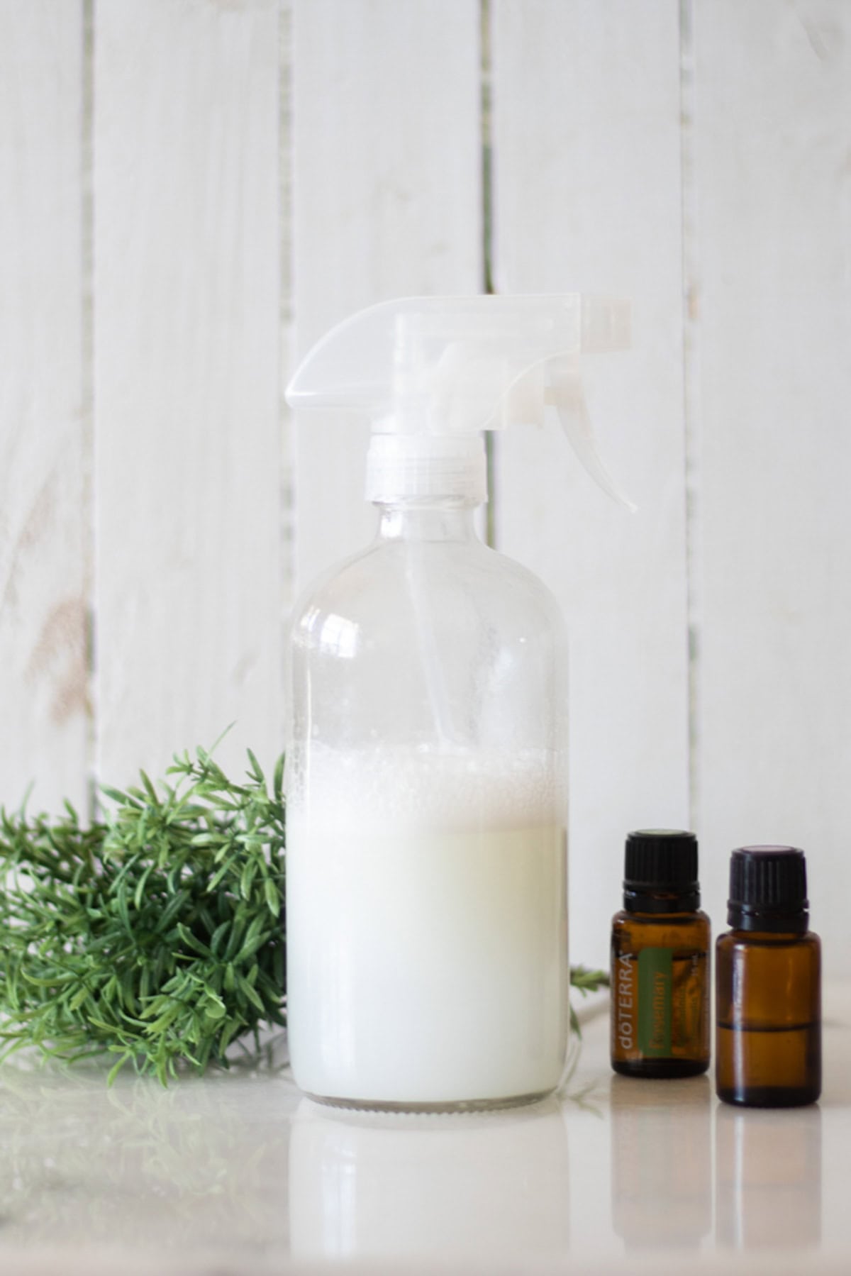 A bottle of hair heat protectant with essential oils and a plant in the background.