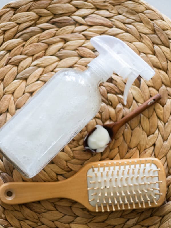 A spray bottle of hair heat protectant with a hair brush on a wicker placemat.