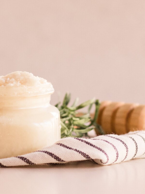 A jar of homemade protein hair mask on a striped towel with a honey stick behind it.