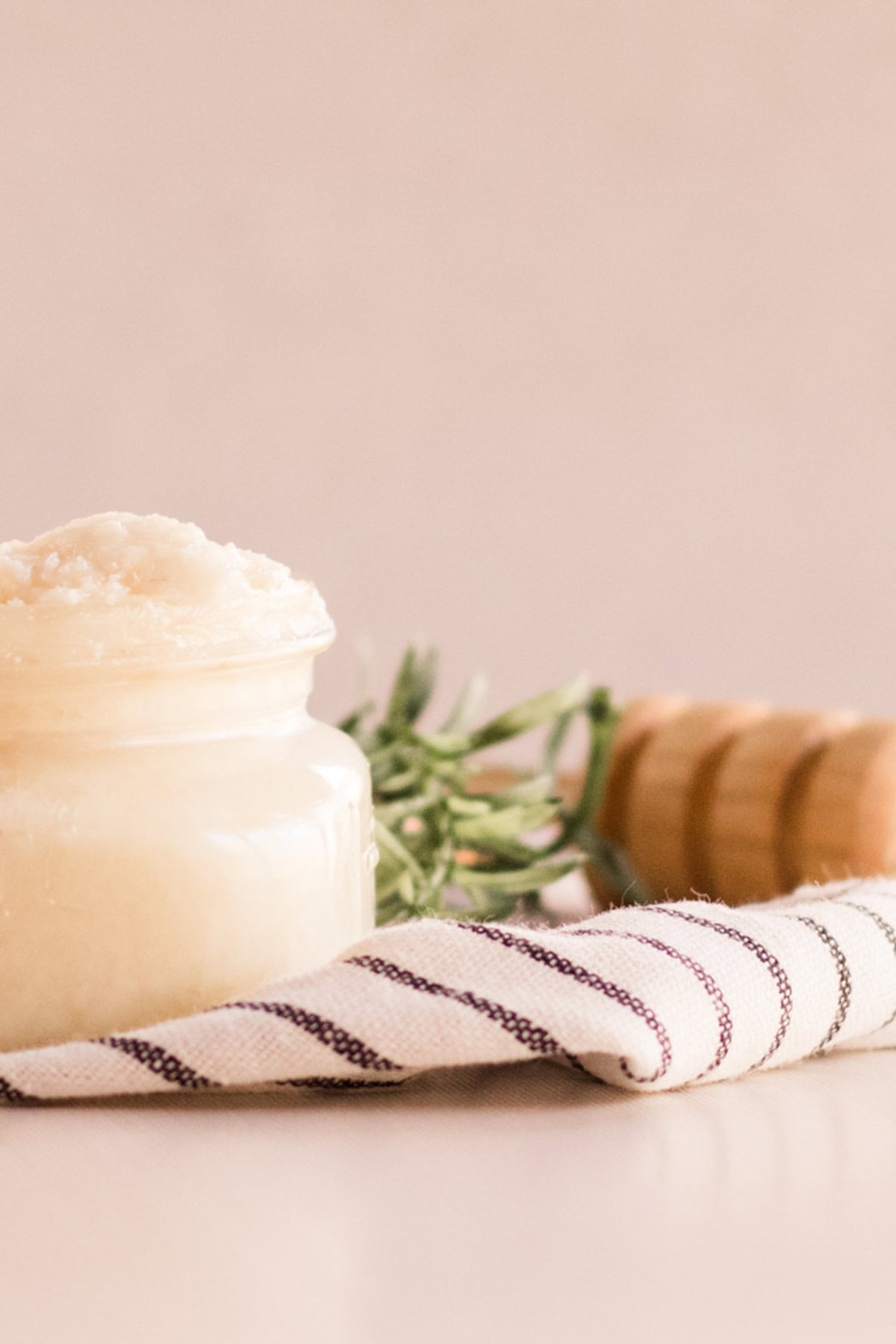 A jar of homemade protein hair mask on a striped towel with a honey stick behind it.