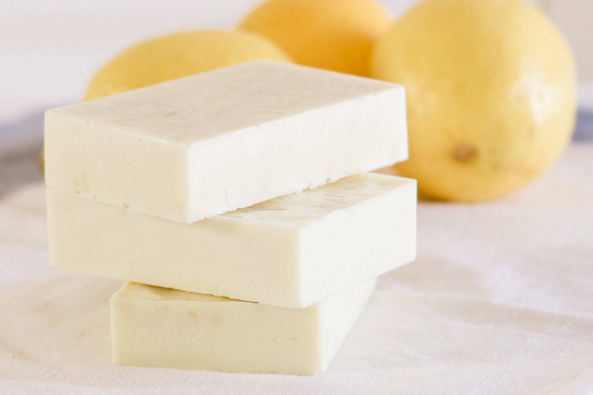 Yellow goat milk soap bars stacked by some fresh lemons. 