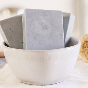 Goat milk soap bars in a white bowl with a scrub brush.