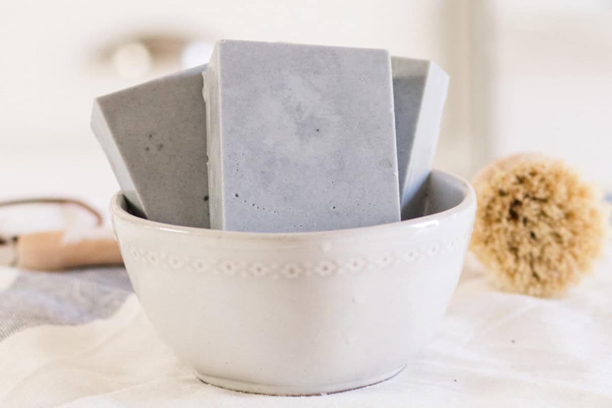 Goat milk soap bars in a white bowl with a scrub brush.