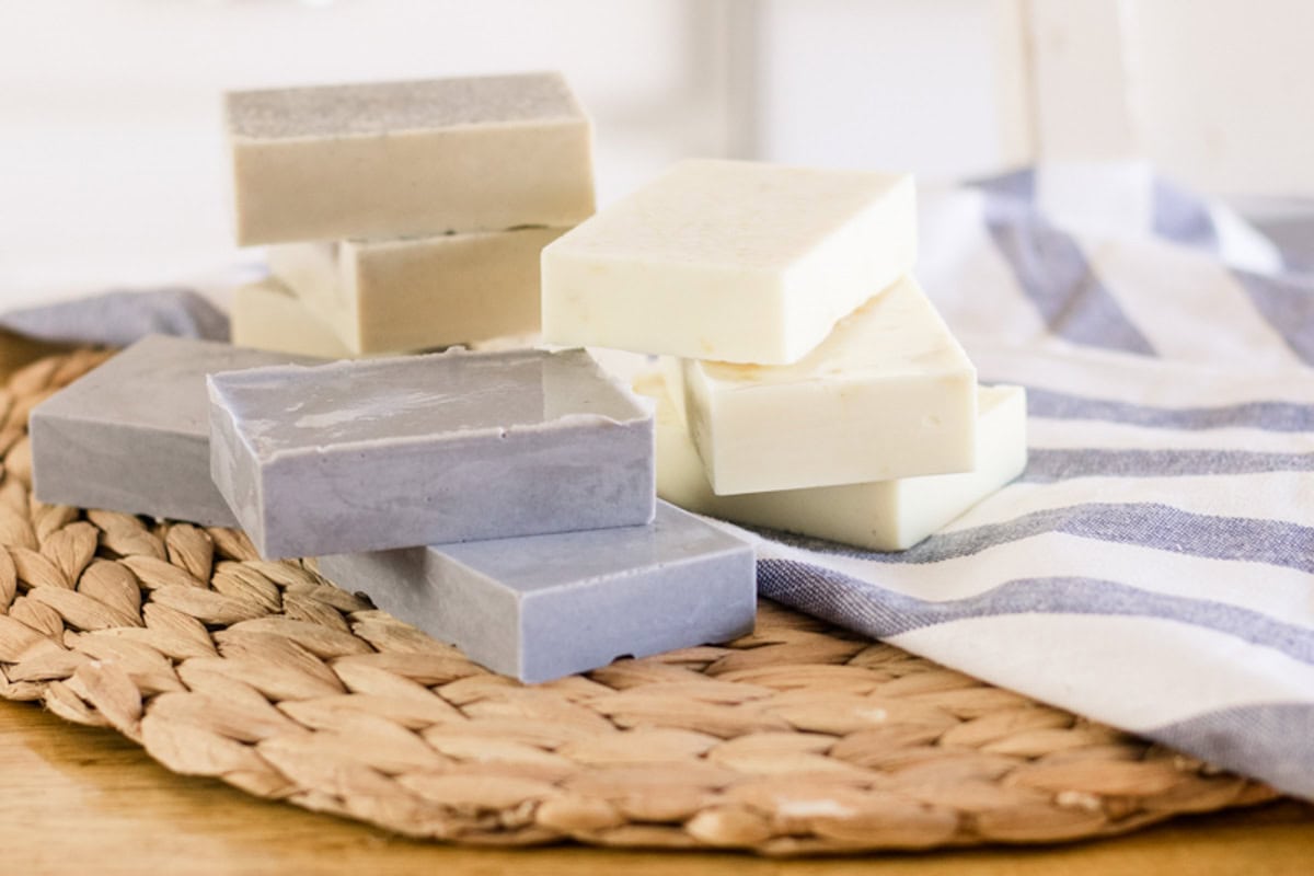 Bars of goat milk soap stacked on a wicker placemat with a blue and white striped towel.