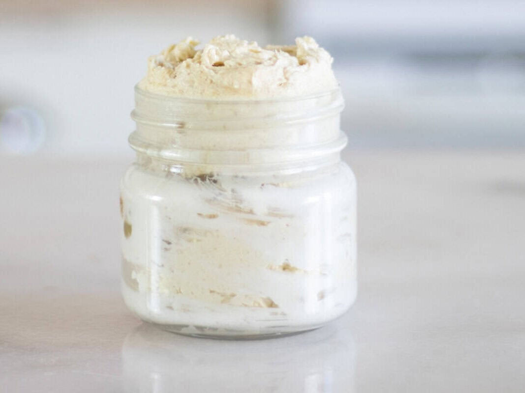 A glass jar of homemade body butter sitting on a kitchen counter.