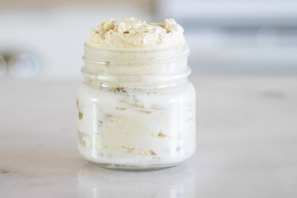 A glass jar of homemade body butter sitting on a kitchen counter.