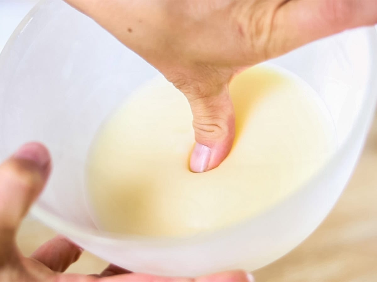 Pressing a finger tip into a bowl of homemade body butter to test its firmness.